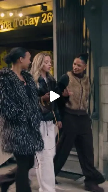 Een still uit de Afroton Ikon-promo: drie vrouwen lopen lachend door een straat, 's avonds.